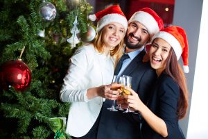Friendly co-workers in Santa caps toasting with champagne by Christmas tree in office