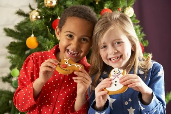 Two Young Children Eating Christmas Treats In Front Of Christmas